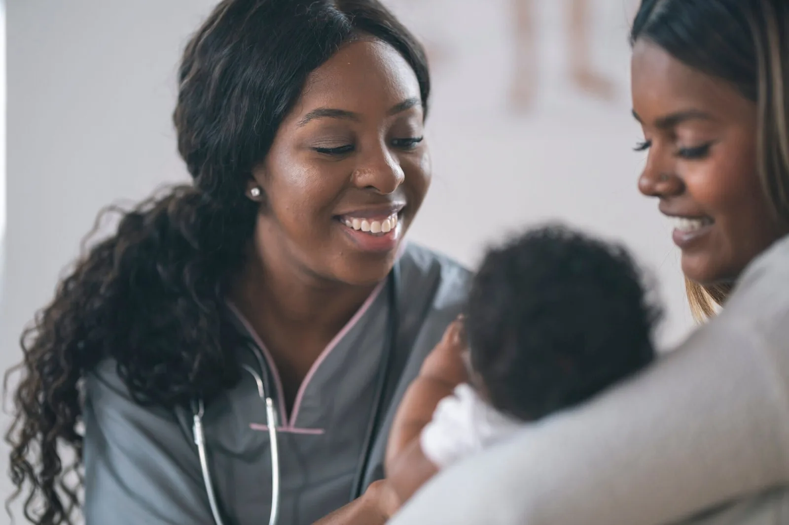 A smiling Malaica clinician with a mother and her baby