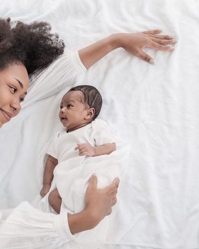 Closeup portrait of beautiful young African American mother day girl kiss healthy newborn baby sleep in bed flat lay copy space. Healthcare medical love black woman lifestyle mother's day, top view